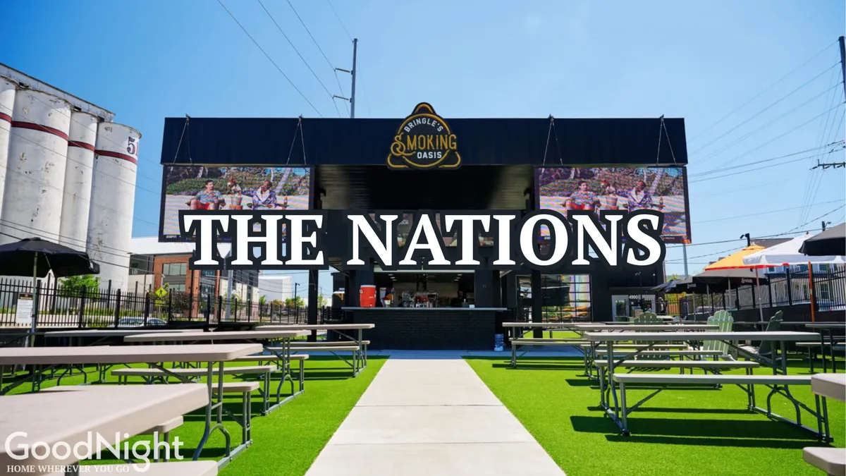 A lively exterior scene of The Nations neighborhood, featuring a large sign that reads 'THE NATIONS', an outdoor seating area with colorful umbrellas, and people enjoying food and drinks at a service window. The setting is festive, with community events and live music suggested by the bustling atmosphere.