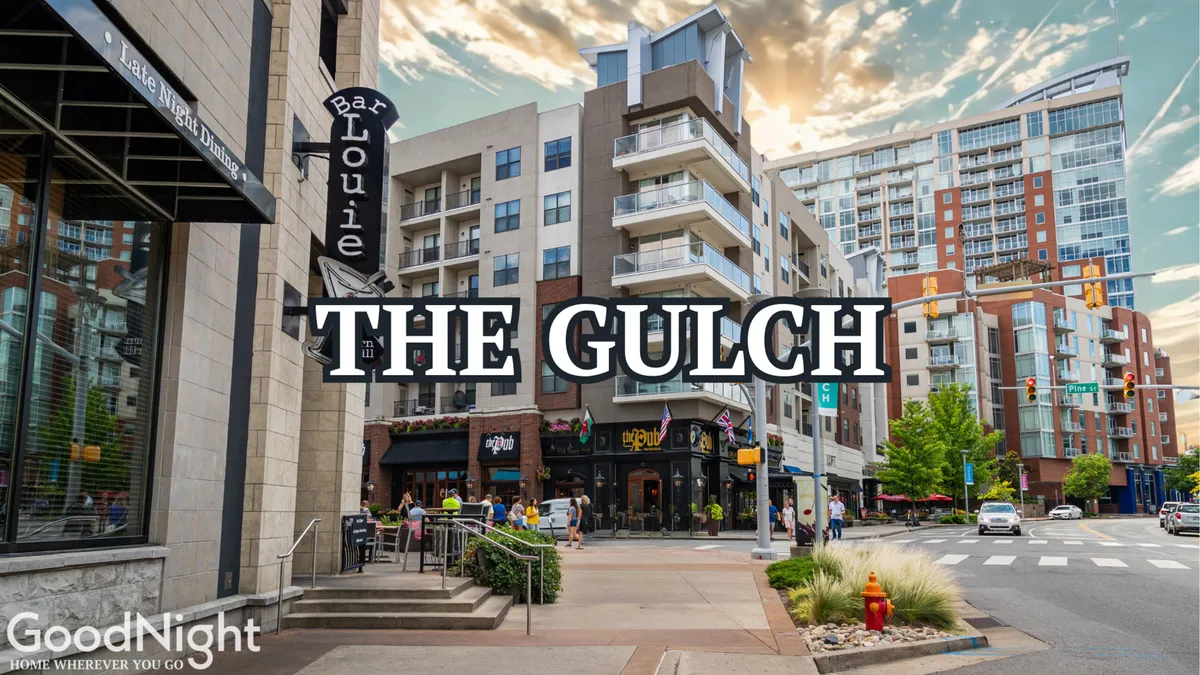 The energetic plaza in The Gulch, featuring the Bar Louie entrance, modern apartments, and people strolling or socializing. City views and the prominent 'The Gulch' sign emphasize the neighborhood's trendy, urban atmosphere and its role as a dining and entertainment hotspot.