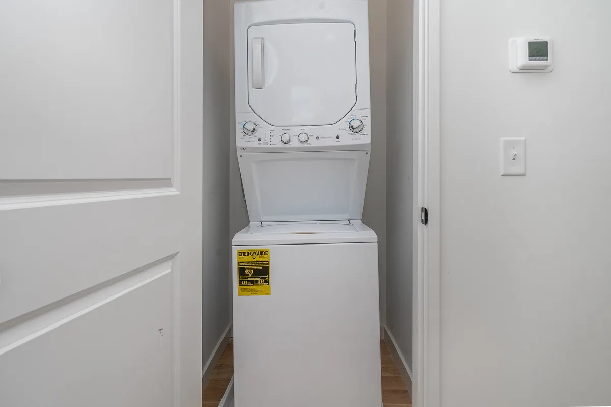 A practical laundry area featuring a stacked washer and dryer unit against crisp white walls, accessed conveniently through an open doorway.